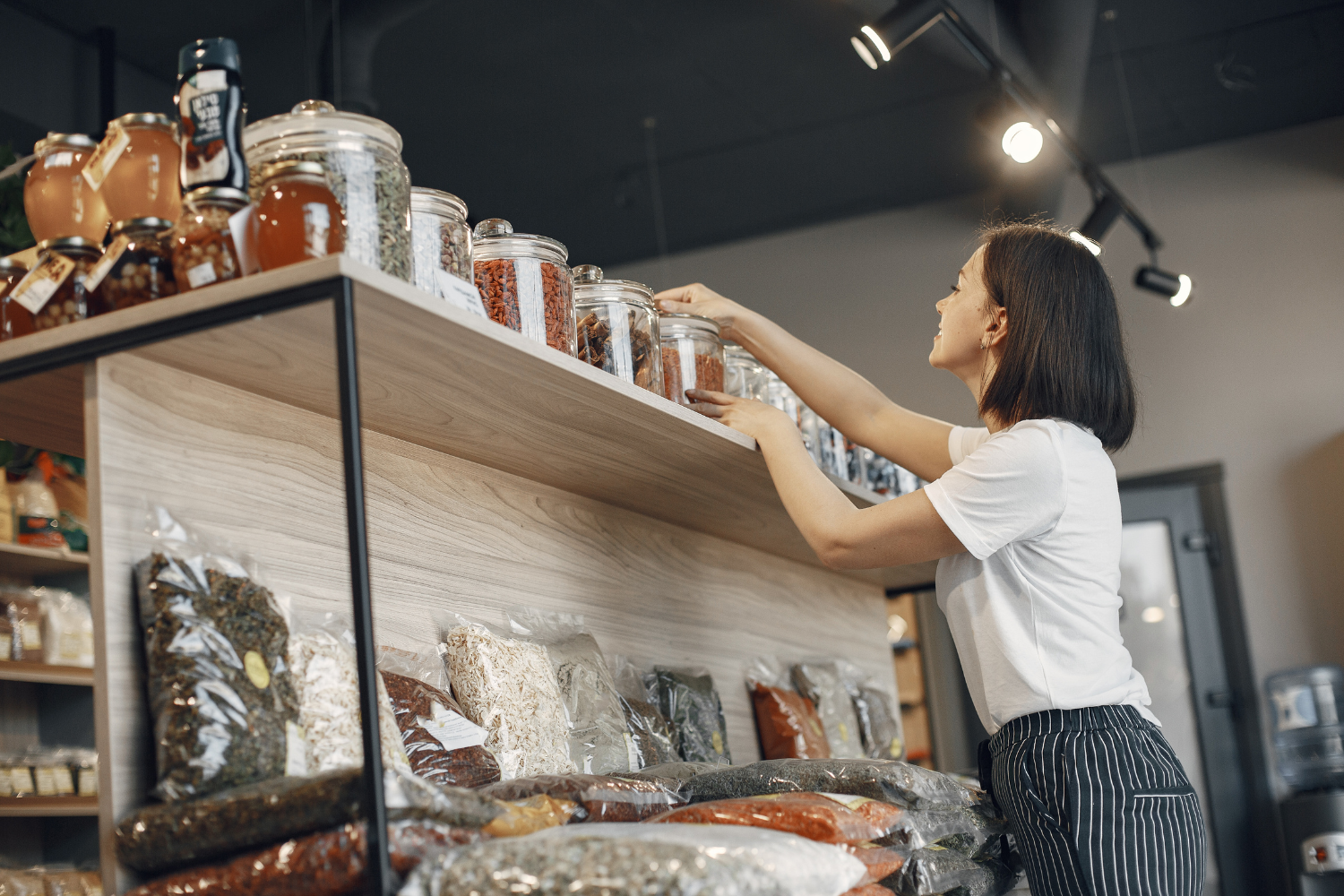 retail merchandiser arranging homeware product display in modern interiors store, clean shelves, commercial product presentation, natural light
